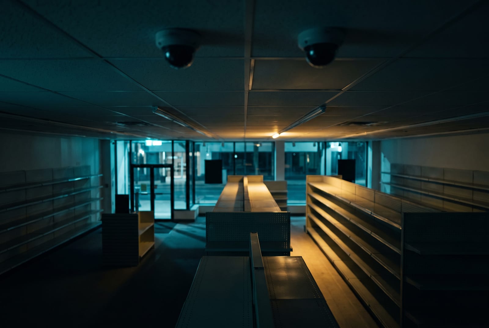 Ceiling-mounted dome cameras above a dark retail sales floor, shelving receding into low warm light